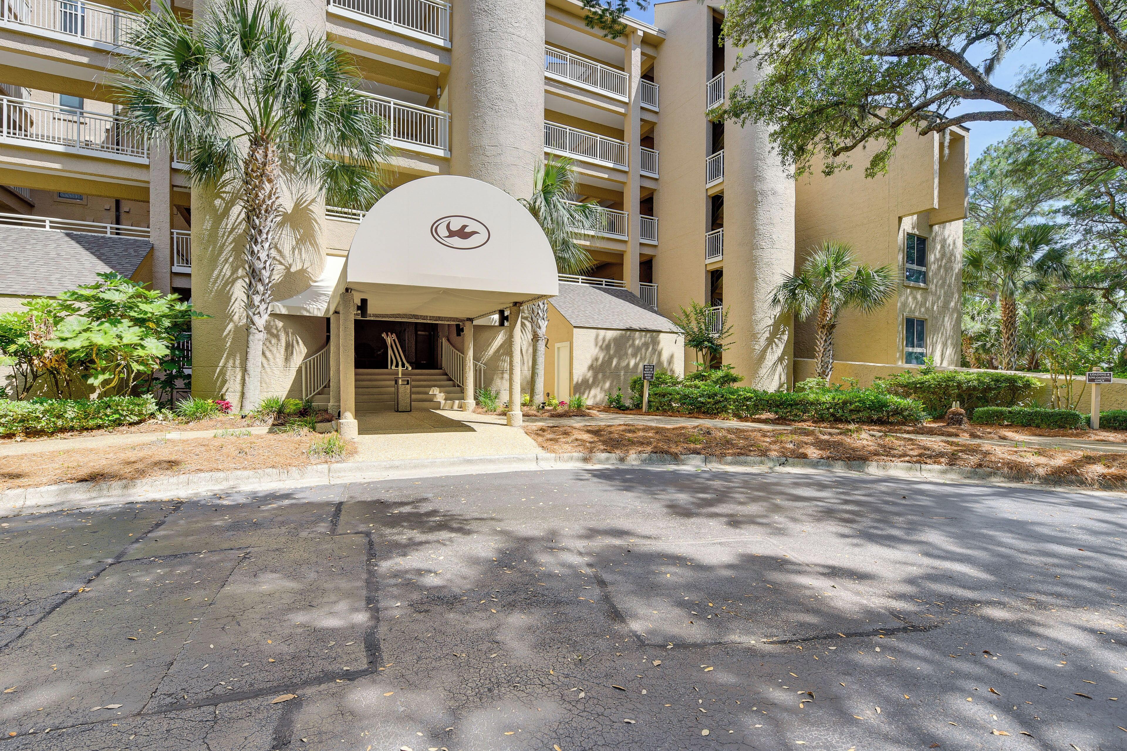 A multi-story building with a central entrance, palm trees, and a clear sky.