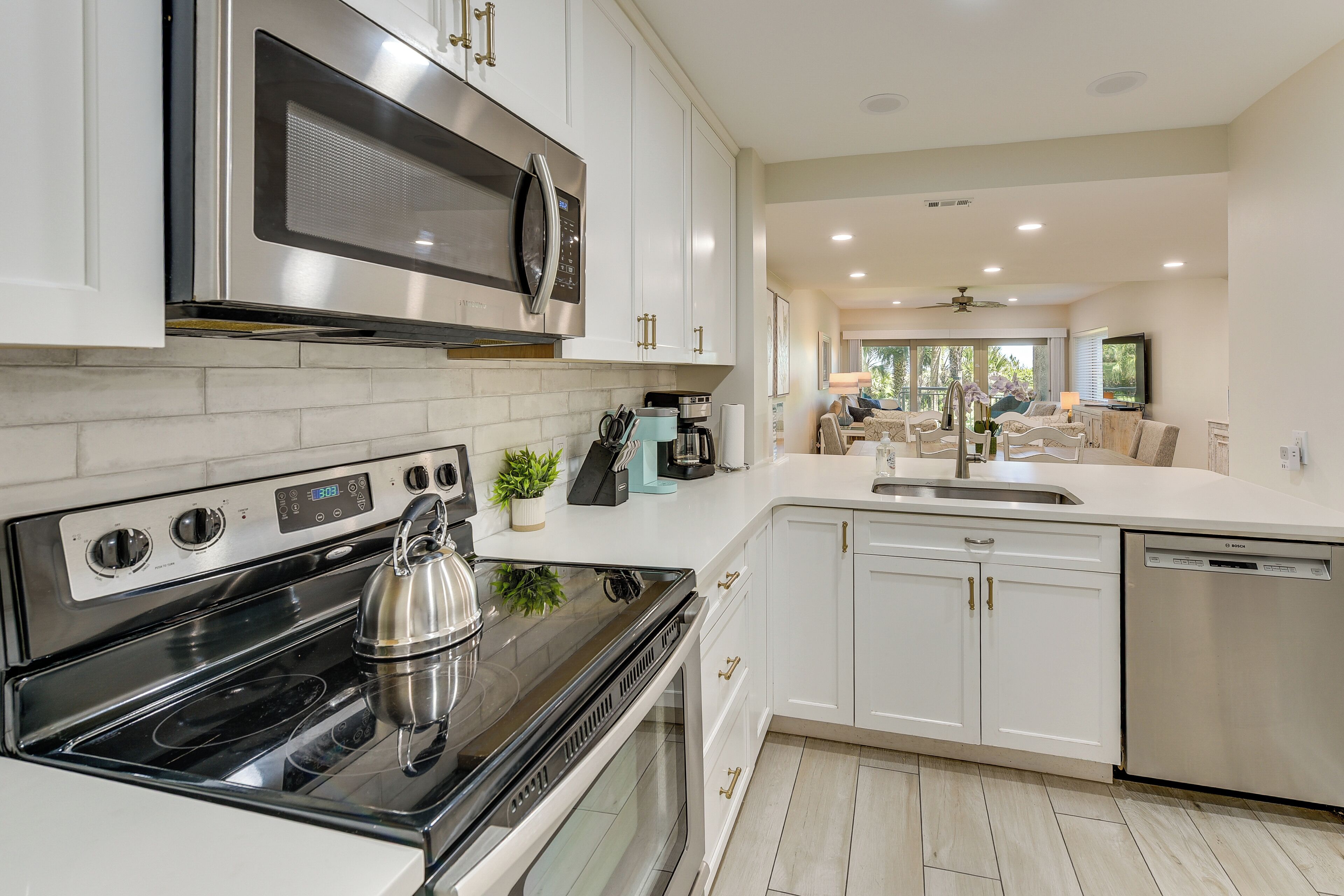 A modern kitchen with stainless steel appliances, white cabinetry, and a view into the living area.