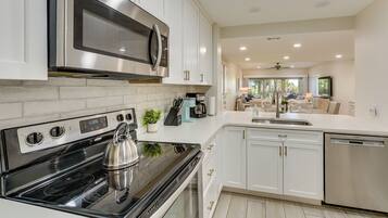 A modern kitchen with stainless steel appliances, white cabinetry, and a view into the living area.