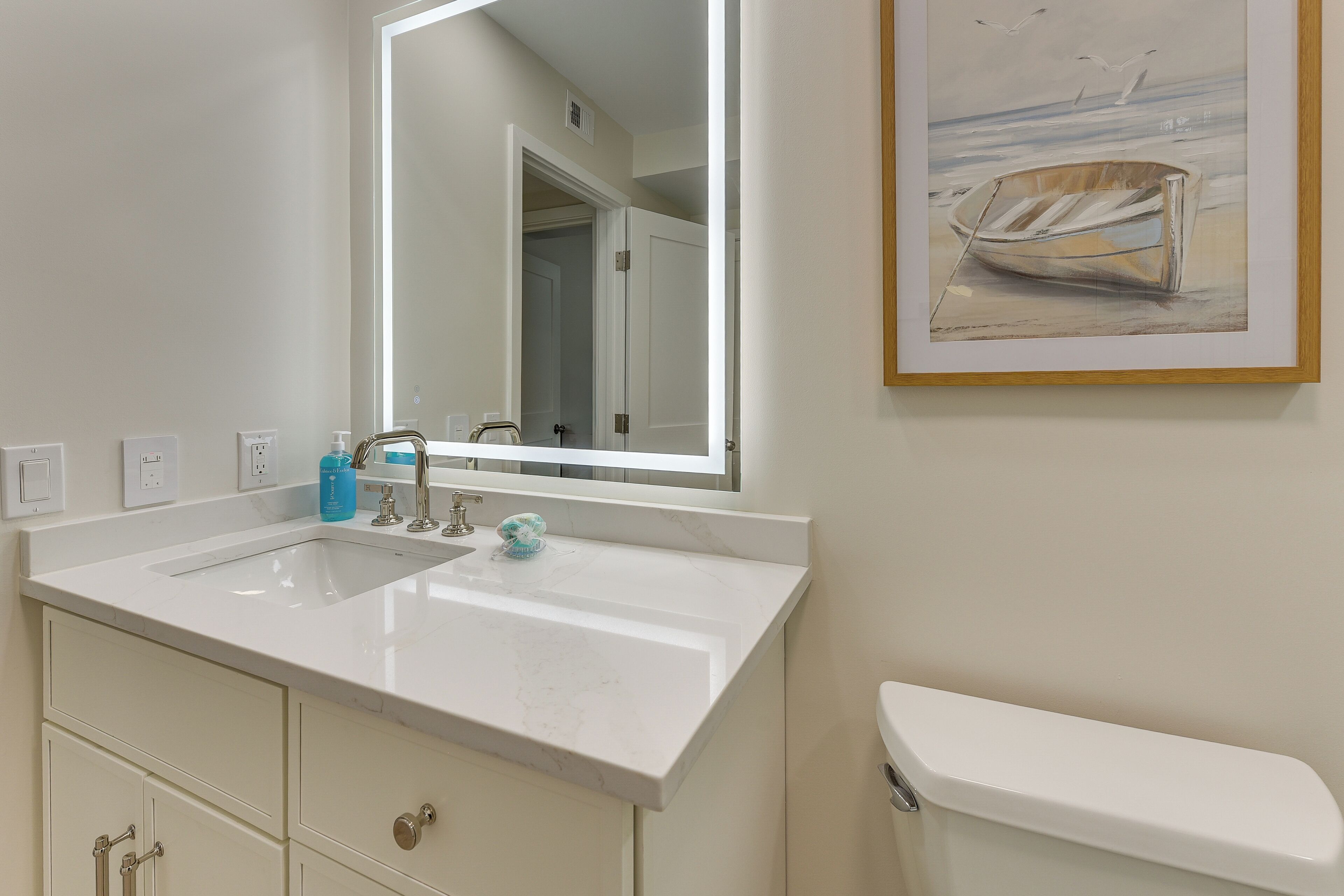 A bathroom with a white sink, a mirror, a toilet, and a framed painting on the wall.