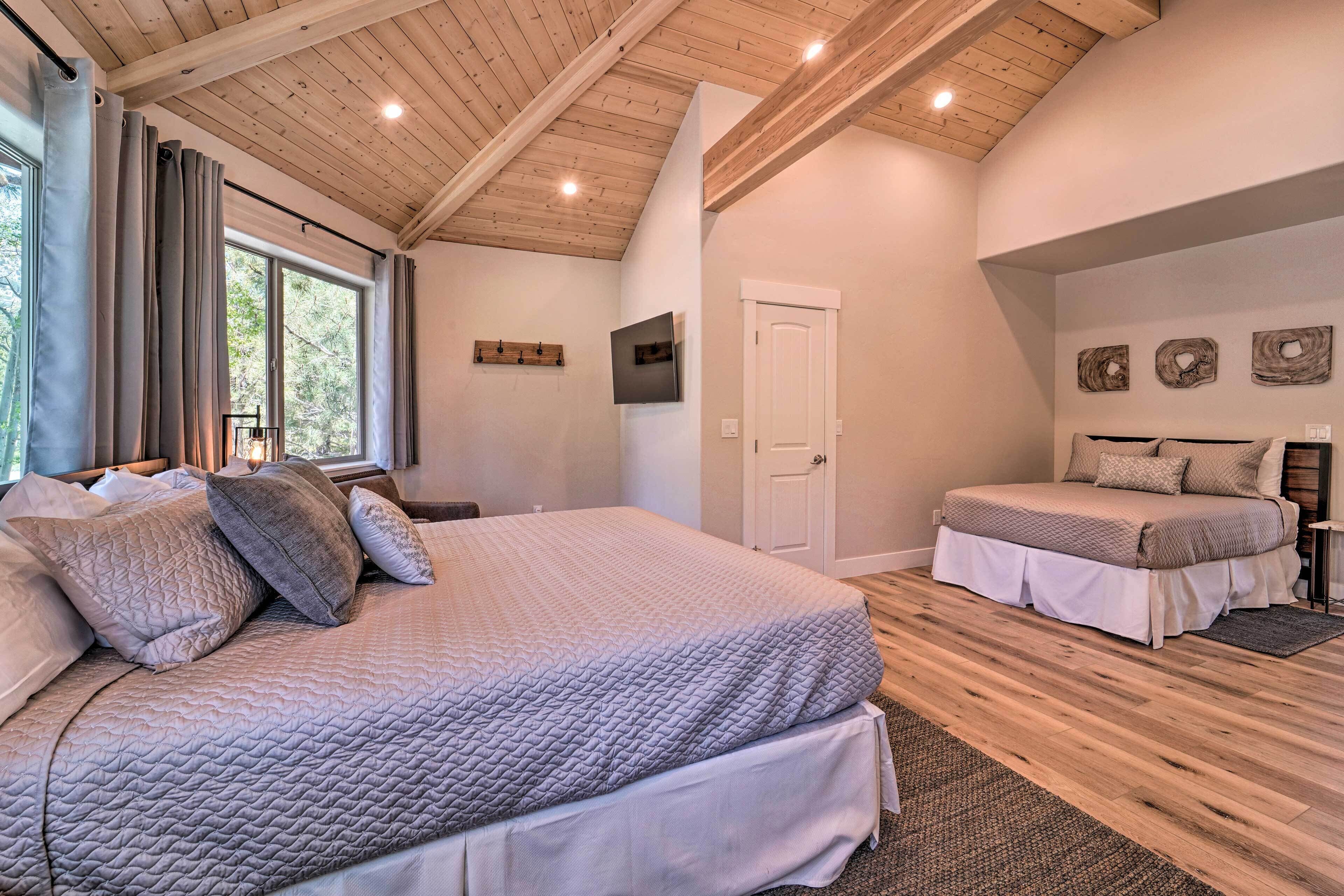 A bedroom with a large bed, a smaller bed, wooden flooring, a door, and a window with curtains.
