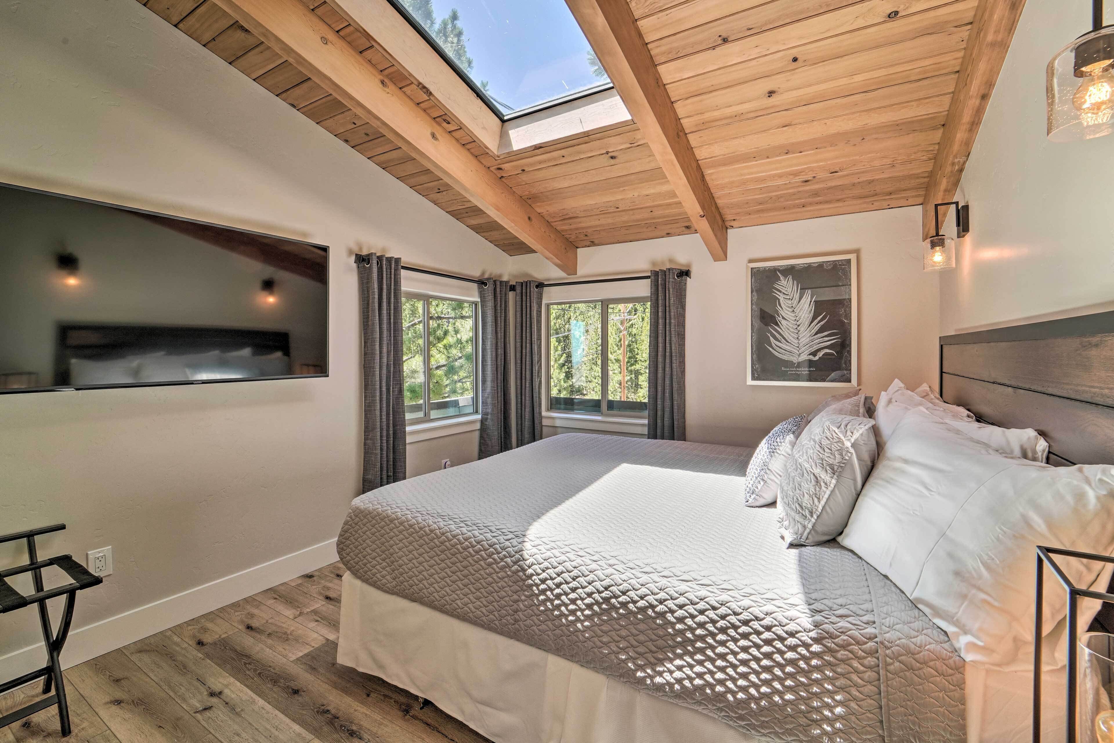 A bedroom with a large bed, skylight, and two windows.