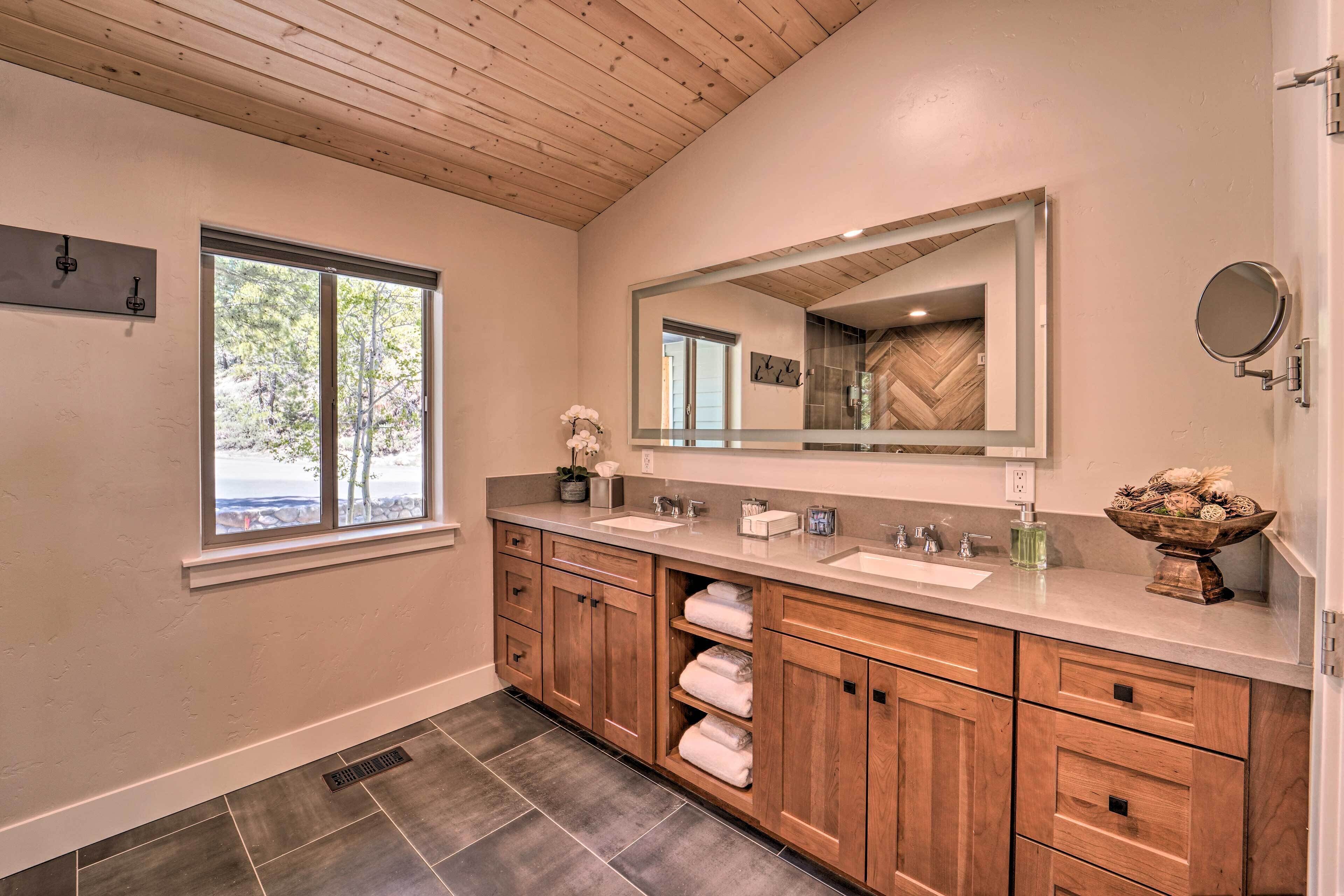 A bathroom with wooden cabinets, a large mirror, and a window with a view of trees.