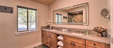A bathroom with wooden cabinets, a large mirror, and a window with a view of trees.