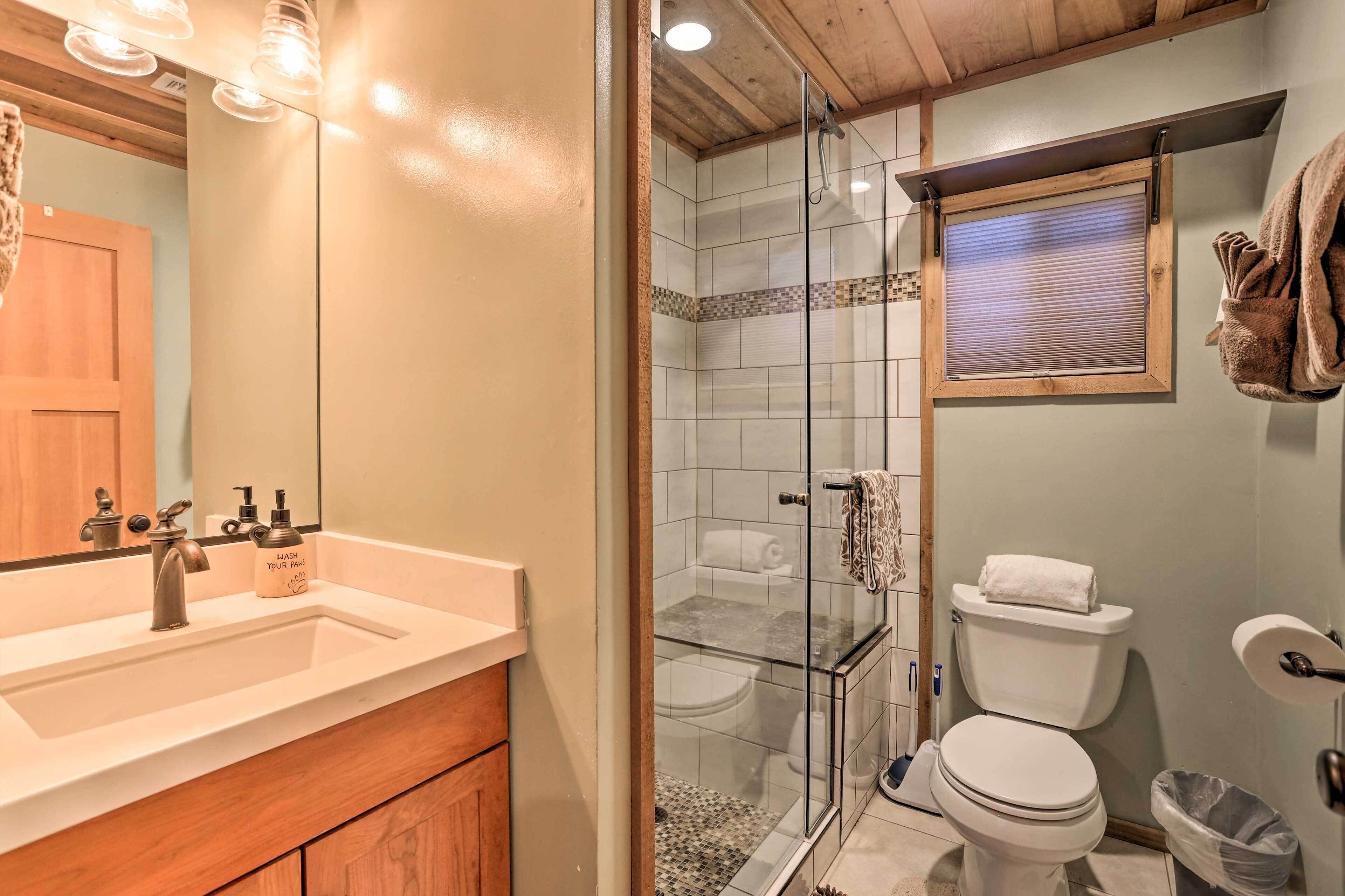 Un baño con cabina de ducha de vidrio, inodoro y lavabo con tocador de madera.