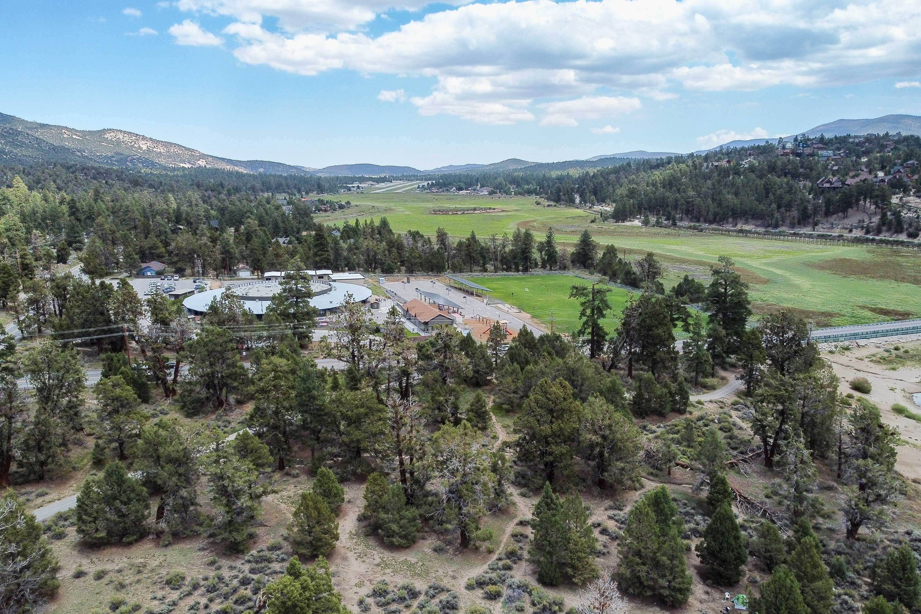A rural landscape with a large open field, a small building complex, and a dense forest.