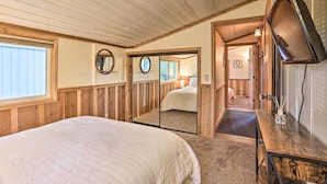 A bedroom with a large bed, wooden walls, a mirror, and a television on a wooden dresser. - Walk to Big Bear Lake: Cozy Cabin w/ Deck (Big Bear Lake)