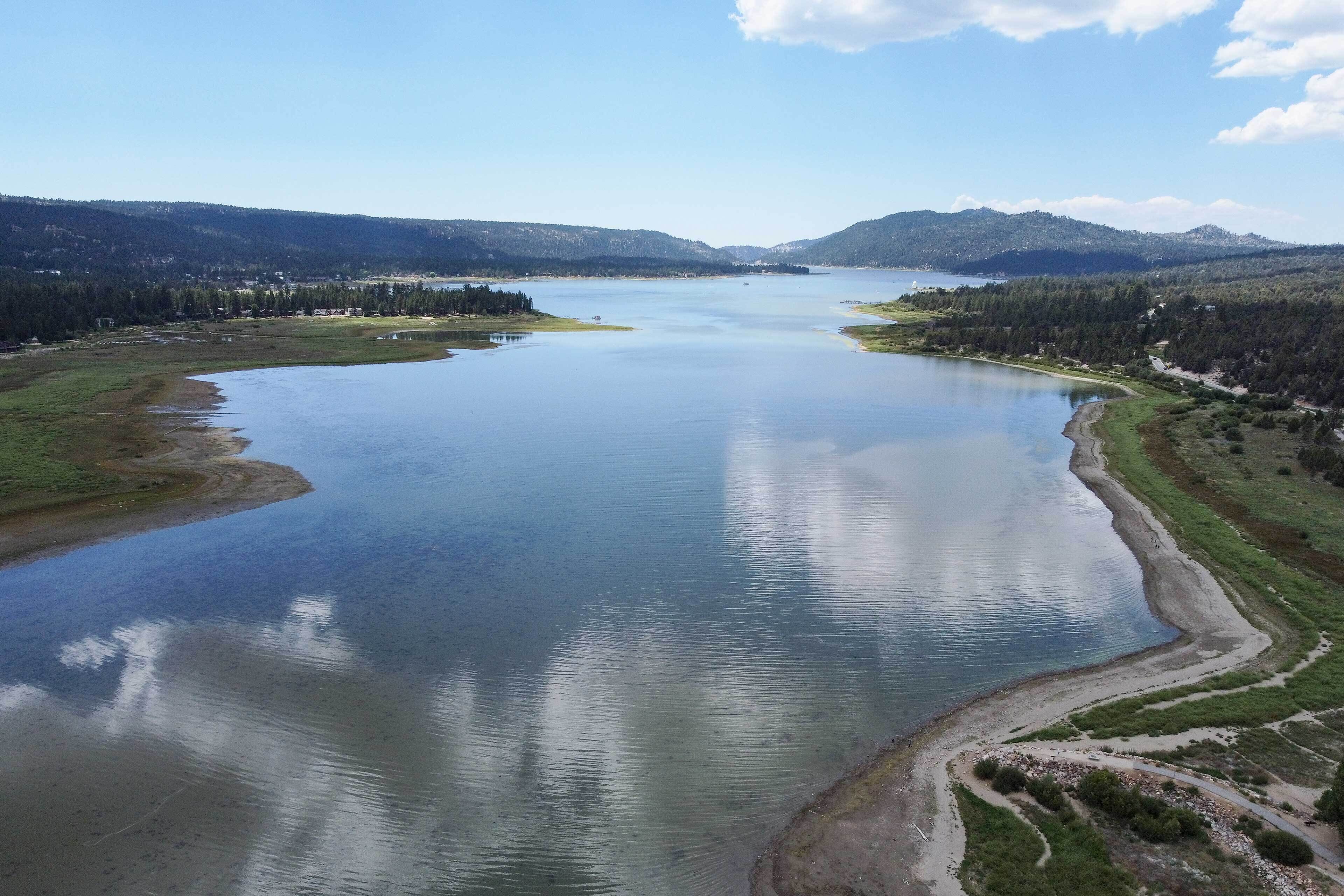 A large lake surrounded by forested hills and a clear sky.