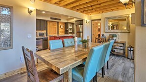 Eine geräumige Küche mit Holzbalken, eine Essecke mit Holztisch und blauen Stühlen sowie eine kleine Küchenzeile.