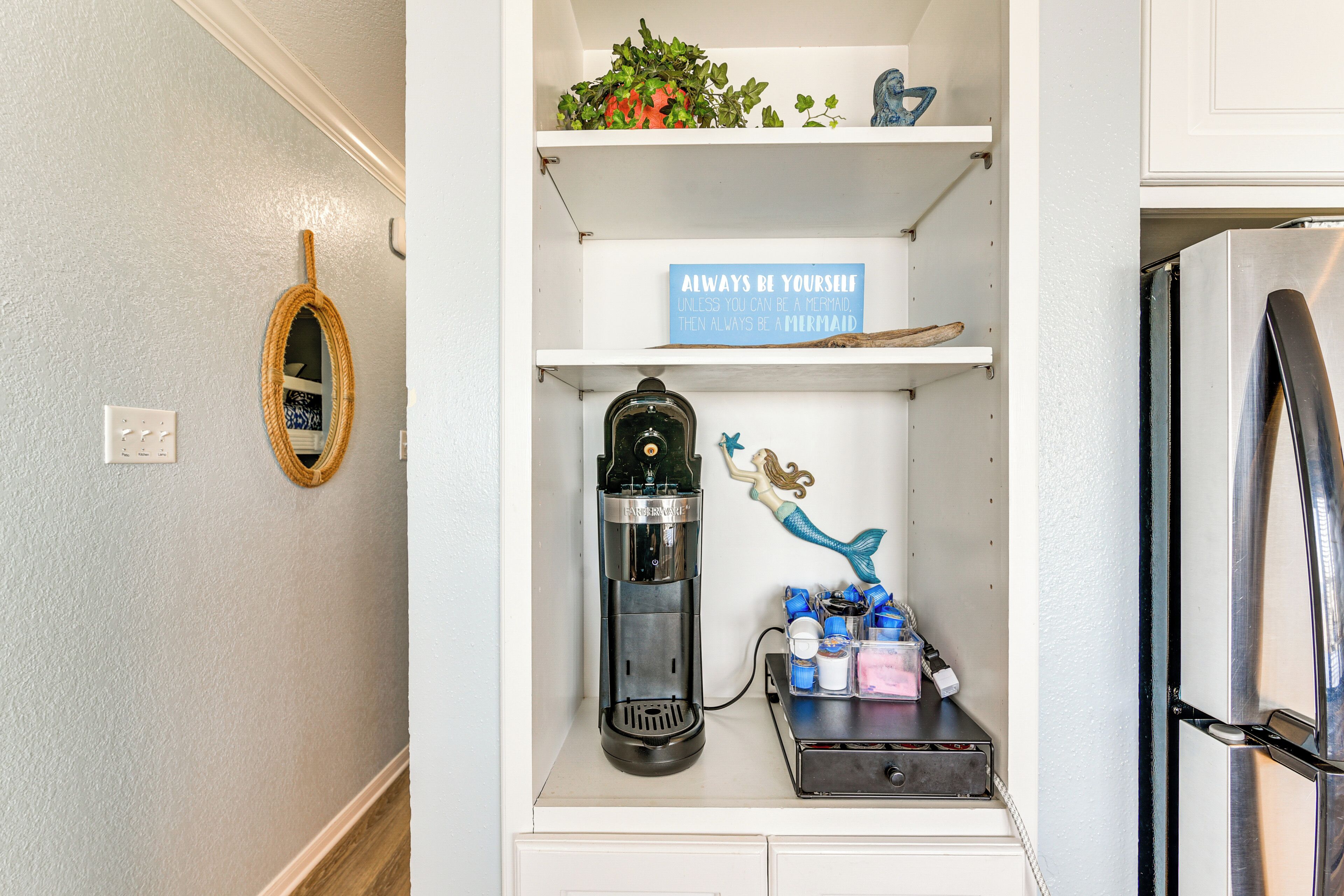 Een keuken met een koffiezetapparaat, een plankje met een zeemeermeidecoratie en een koelkast.