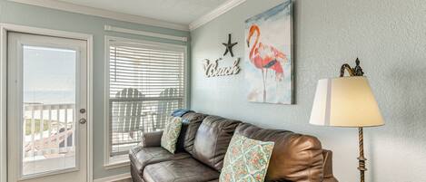 A living room with a brown leather sofa, patterned cushions, a starfish wall decoration, a flamingo painting, and a lamp.