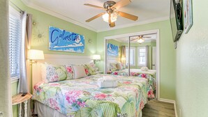 Une chambre avec deux lits, une literie à motifs floraux, des ventilateurs de plafond et des œuvres d’art accrochées aux murs.