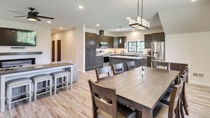 A modern kitchen with dark cabinets, a central island, and a dining area with a large table and chairs. - Modern Kalispell Retreat: 37 Mi to Glacier NP (Kalispell)