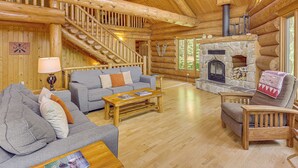A log cabin interior with a stone fireplace, wooden staircase, and a cozy seating area. - Waterfront Escape on Caribou Lake: Dock + Fire Pit (Lutsen)