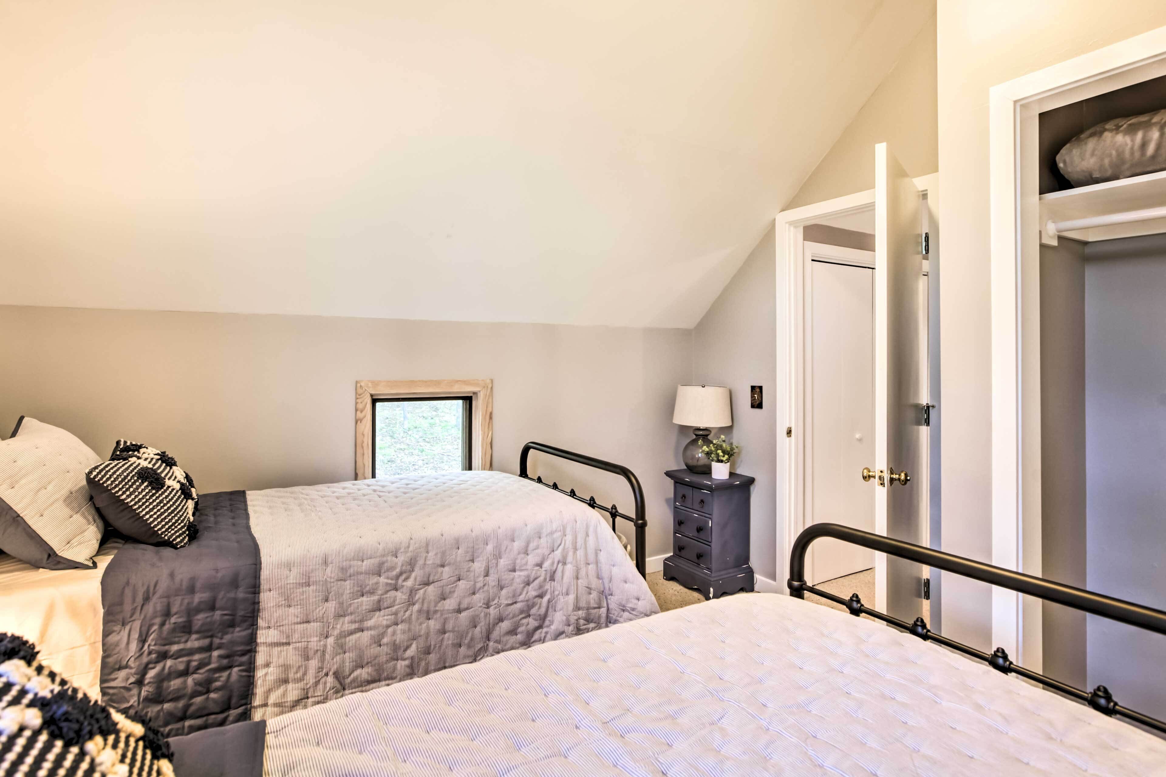 A bedroom with two beds, a dresser, a lamp, and a door leading to another room.