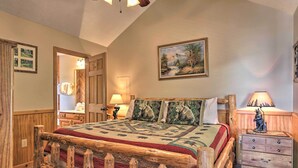 A wooden bed with a quilt, a nightstand with a lamp, and a painting on the wall. - Smoky Mountain Retreat w/ Hot Tub, Arcade Games (Sevierville)