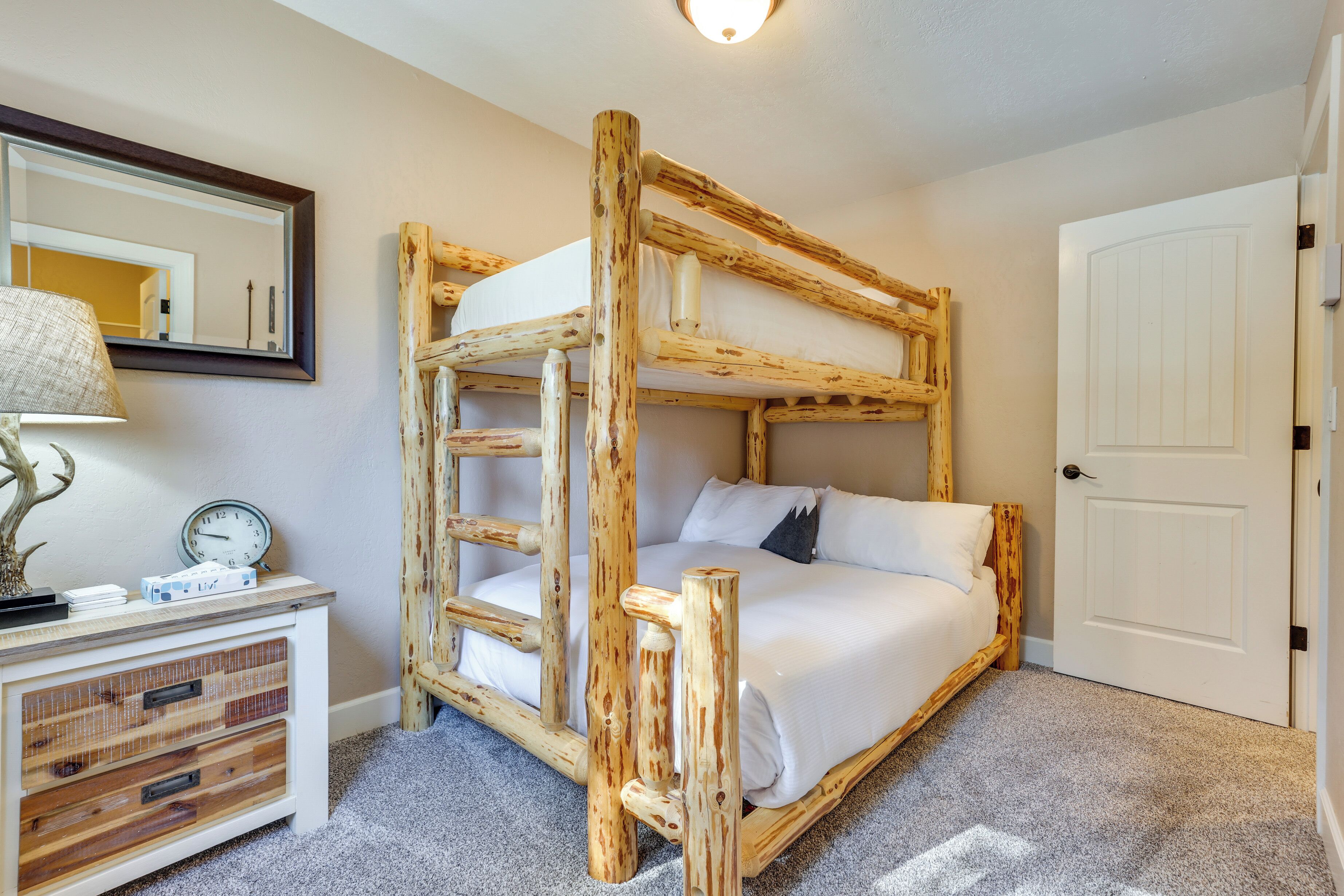 Een stapelbed met houten frame, een nachtkastje met lamp en een klok.