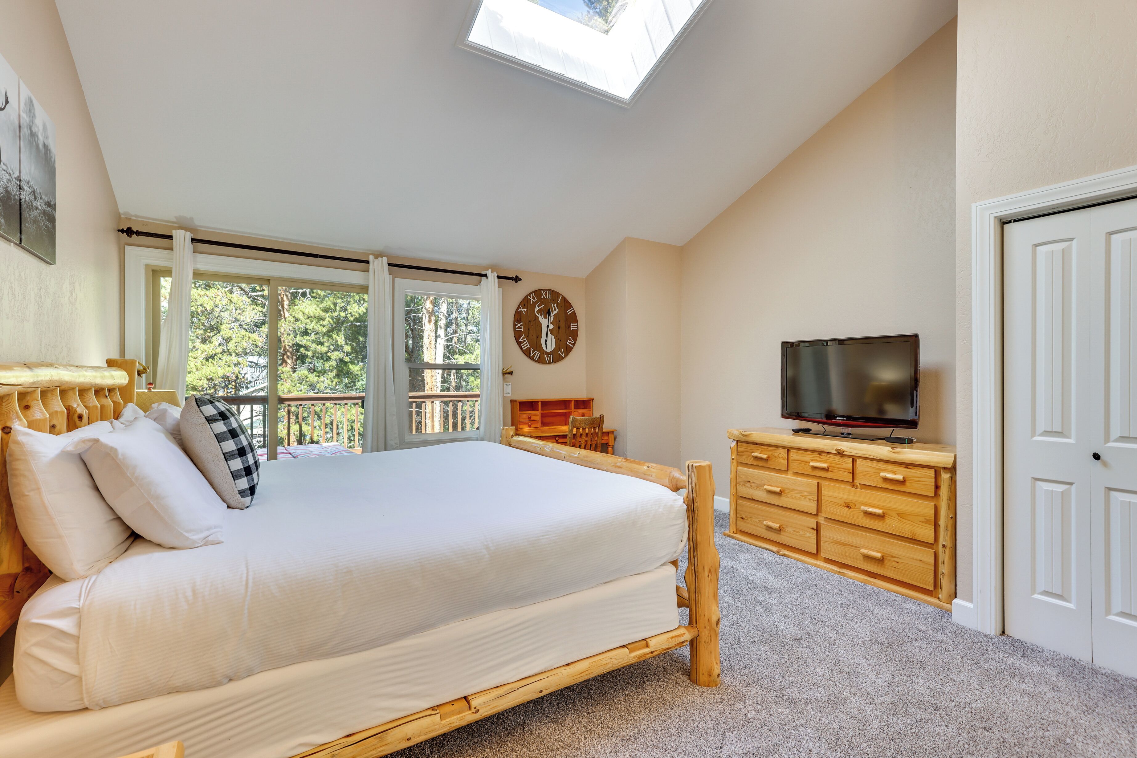 A bedroom with a large bed, wooden dresser, TV, and a clock on the wall.
