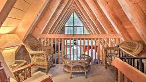 A cozy attic room with wooden beams, wicker furniture, and a large window offering a view of trees. - A-frame Cabin w/ Hot Tub < 1 Mi to Ober Gatlinburg (Gatlinburg)