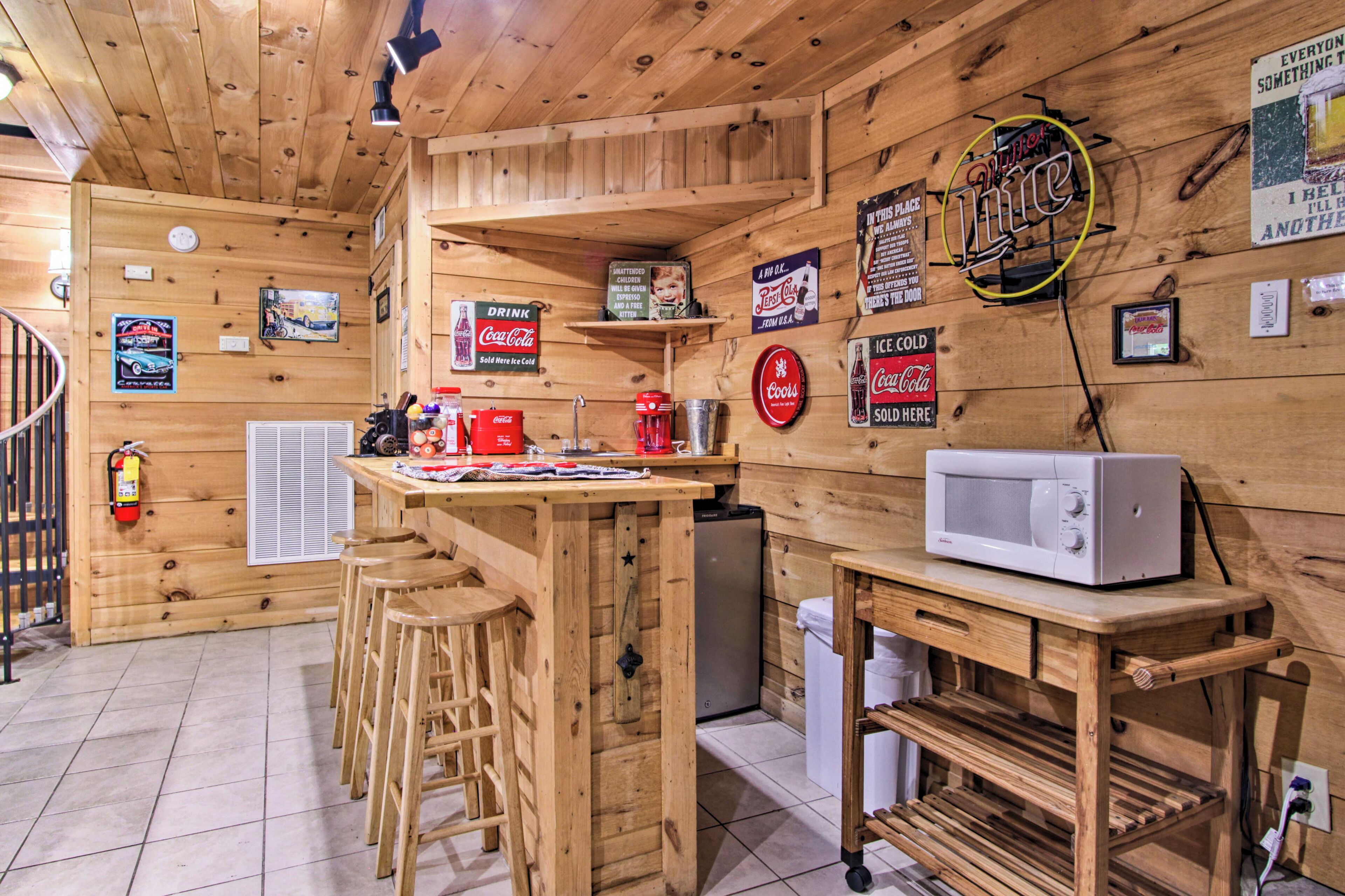 Un interior de madera con una zona de bar, taburetes, un microondas y varios carteles, incluyendo Coca-Cola y un letrero de neón.