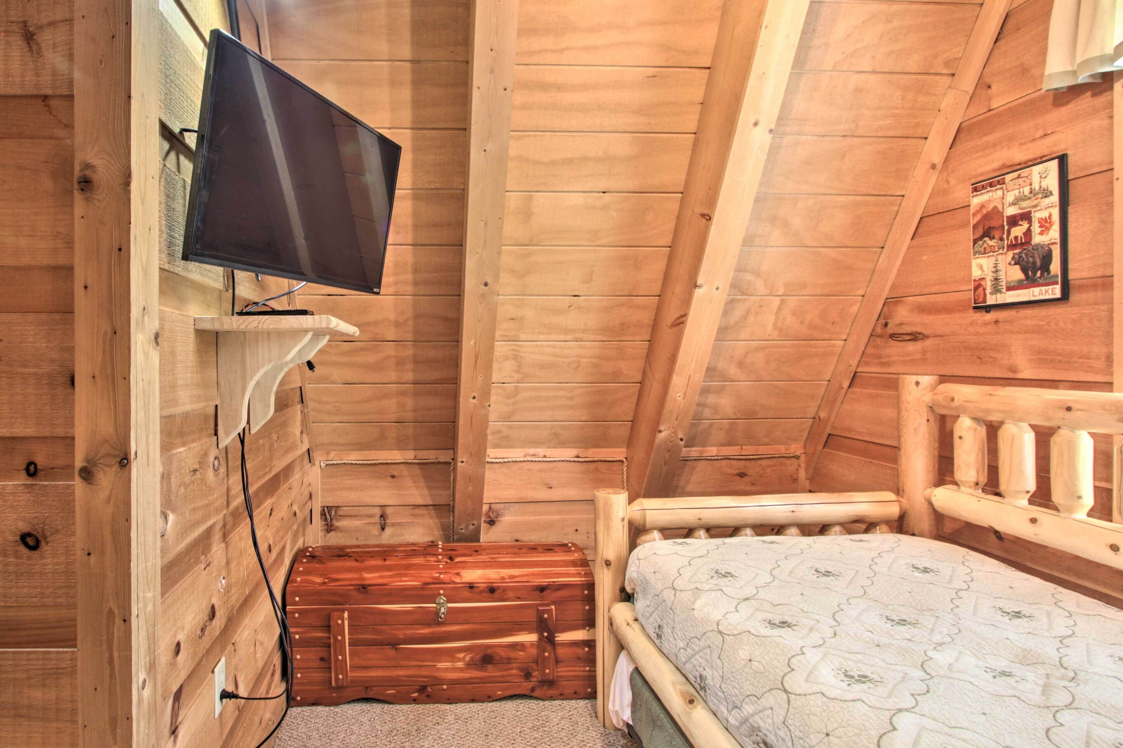 Ein Zimmer einer Holzhütte mit einem Bett, einem an der Wand befestigten Fernseher und einer Holzkommode.