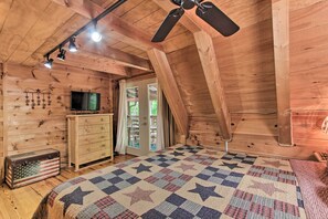 A log cabin bedroom with a star-patterned quilt, wooden dresser, and a television on a wooden cabinet.