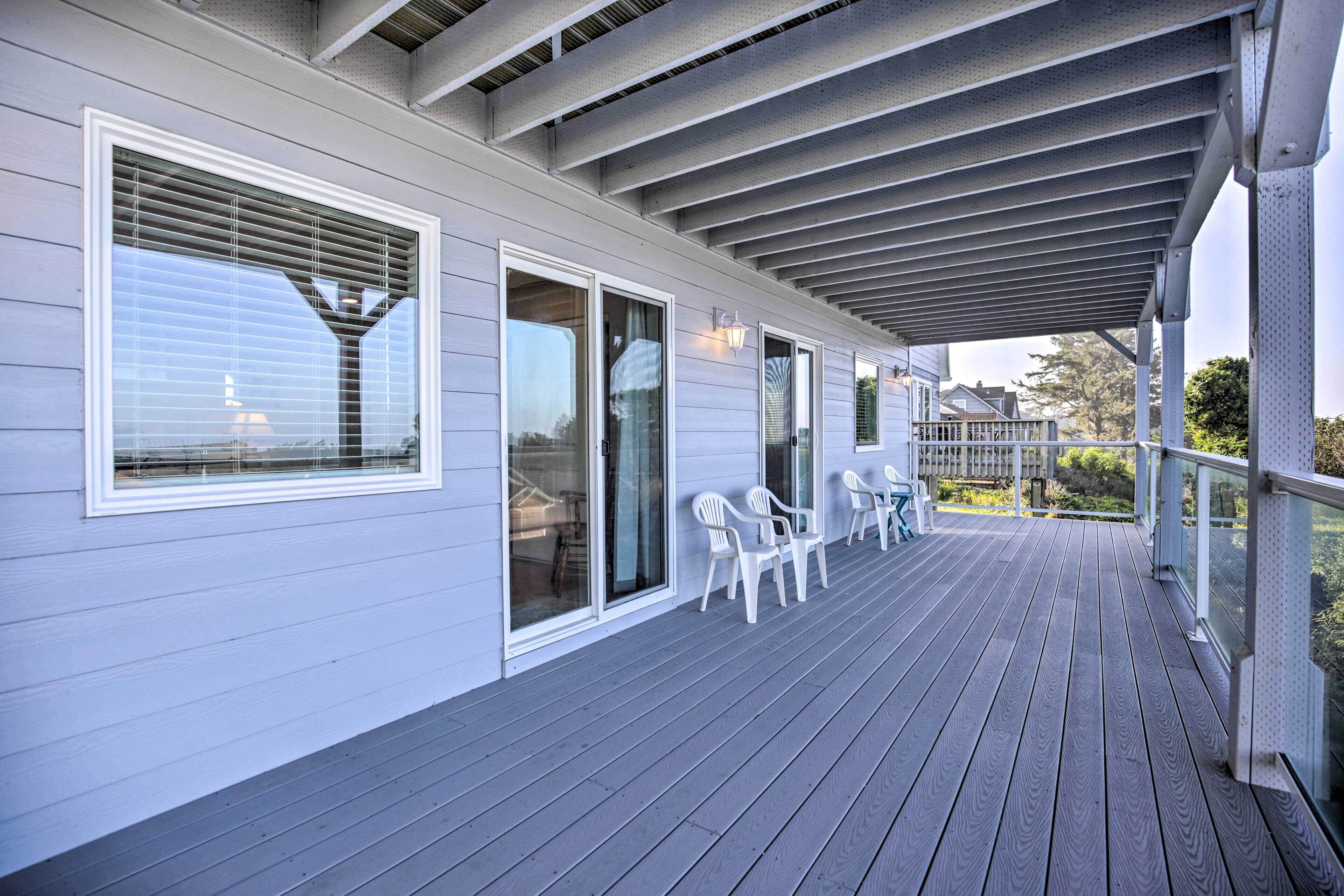A covered porch with a railing, a seating area with chairs, and a view of the surrounding neighborhood.
