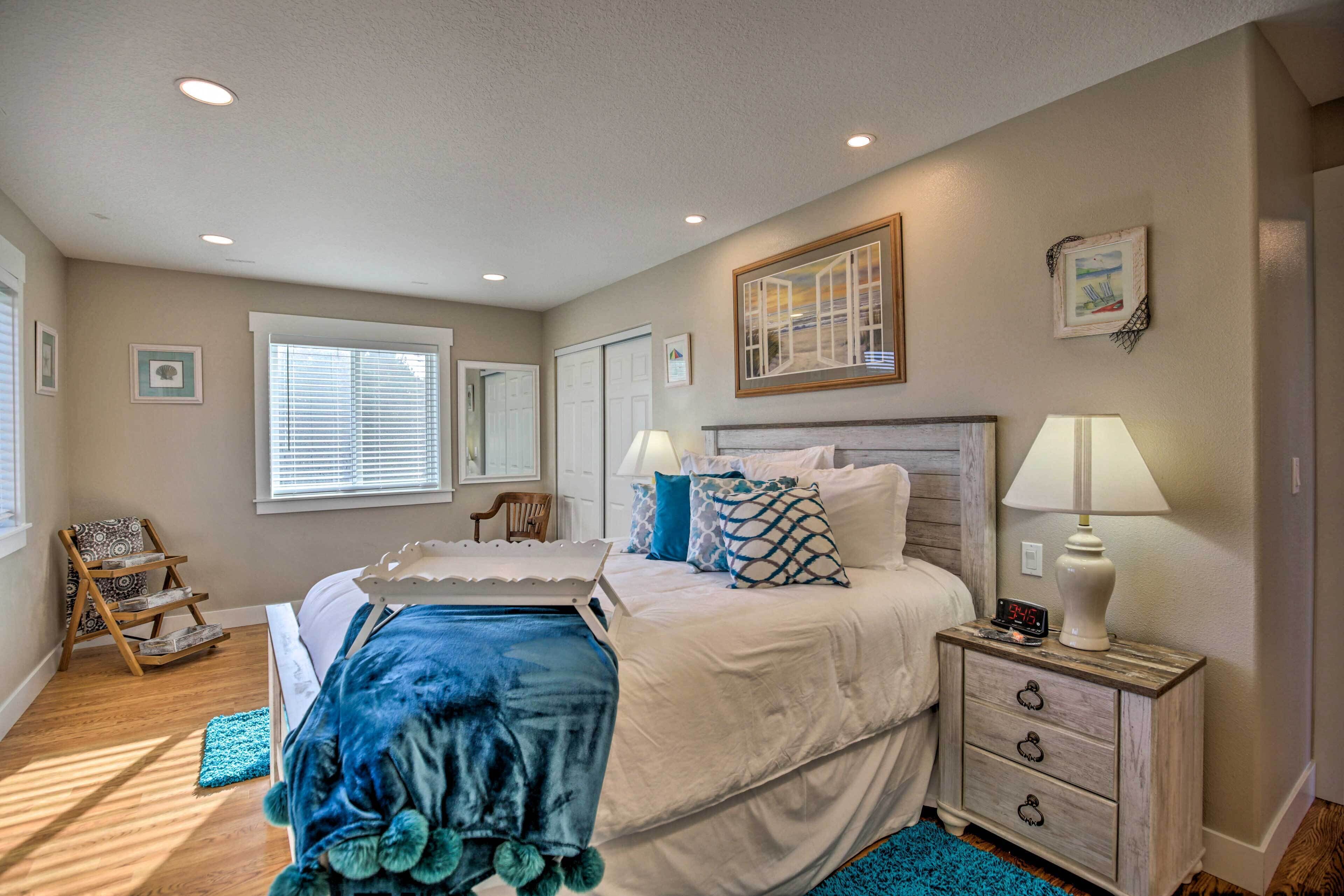 A bedroom with a bed, bedside table, nightstand, and a window with blinds.