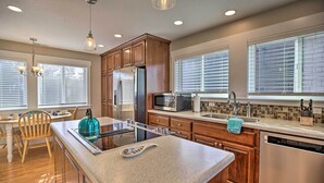A modern kitchen with wooden cabinets, stainless steel appliances, a large island, and a view of the outdoors through large windows. - Ocean-view Lincoln City Retreat w/ 3 Viewing Decks (Lincoln City)