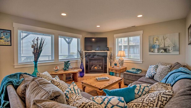 A cozy living room with a fireplace, comfortable seating, and large windows. - Ocean-view Lincoln City Retreat w/ 3 Viewing Decks (Lincoln City)