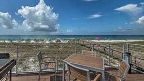 Una terrazza con tavolo e sedie che si affaccia su una spiaggia con ombrelloni e una passerella in legno.