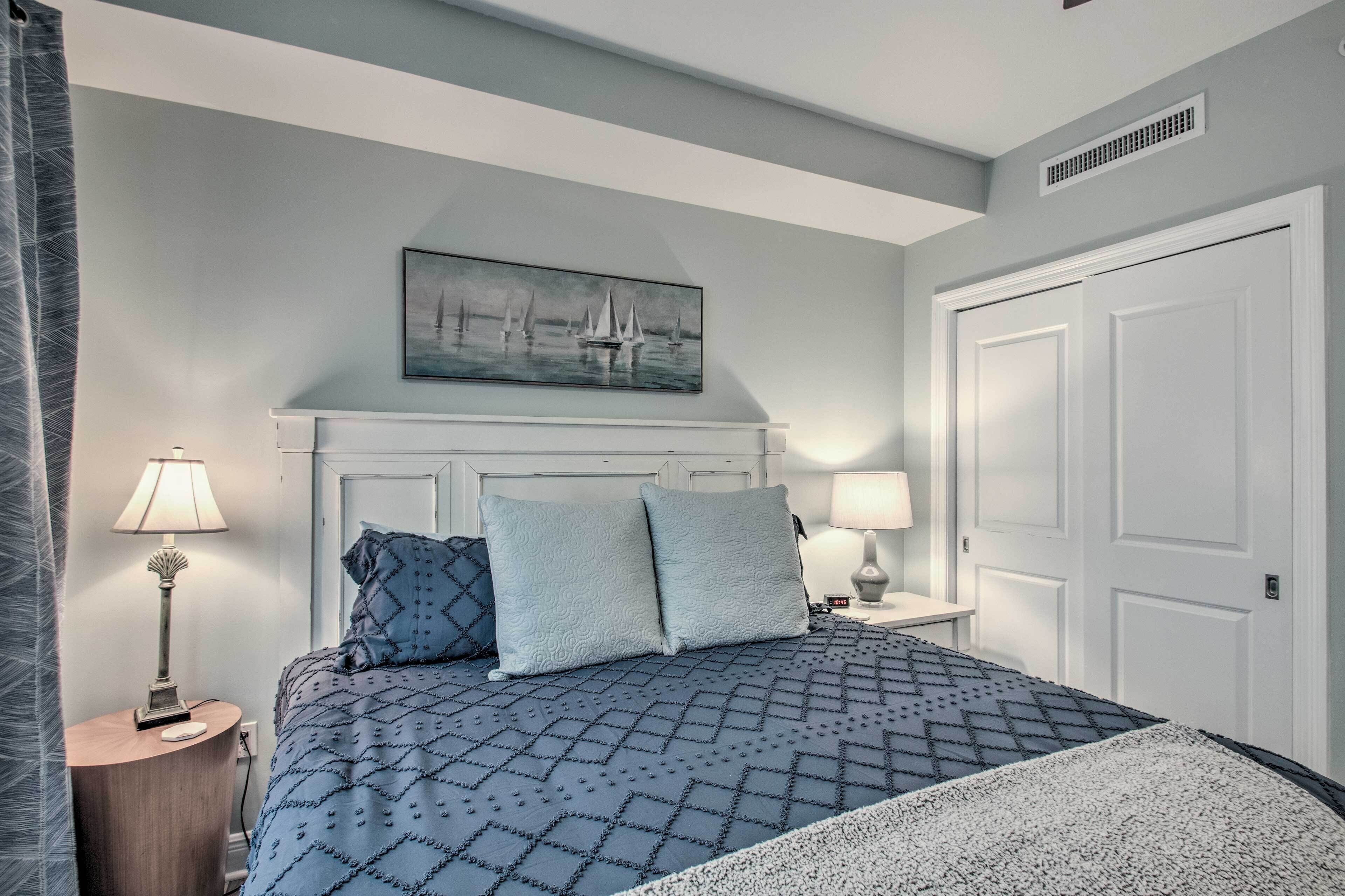 A neatly arranged bedroom with a bed, two bedside lamps, a painting above the bed, and a closed door.