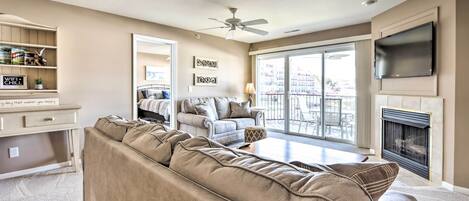 A living room with a beige sofa, a TV mounted on the wall, a fireplace, and a balcony with a view of the city.