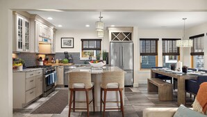 Una cocina moderna con armarios blancos, un refrigerador de acero inoxidable y un comedor con mesa de madera y taburetes de bar.
