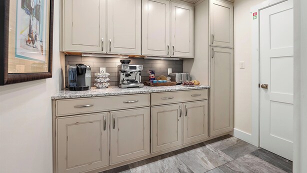 Una cocina con gabinetes color beige, una encimera con electrodomésticos y una puerta con señal de salida de emergencia.