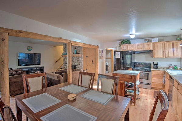 A spacious living area with a wooden dining table, chairs, a television, and a stone fireplace. - 7 Mi to Heavenly Ski Resort: Cozy Tahoe Cabin (South Lake Tahoe)