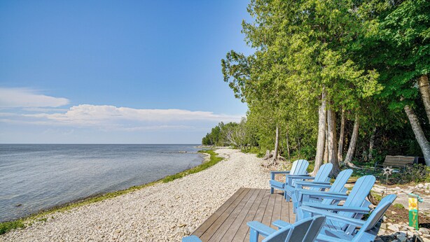 Une terrasse en bois avec des fauteuils Adirondack bleus, donnant sur une plage de galets et l’océan.