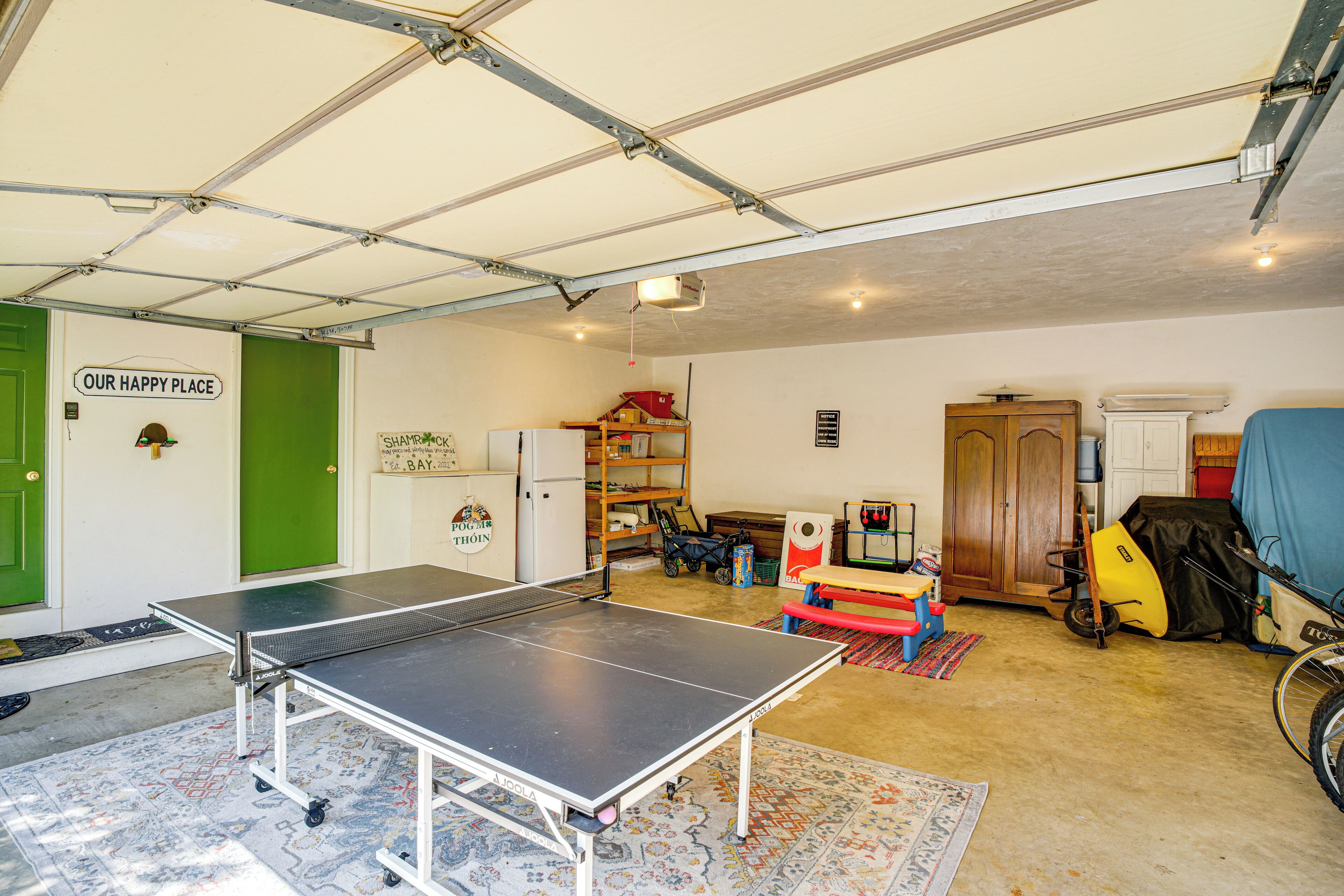 Eine Garage mit Tischtennisplatte, einer grünen Tür und einem Schild, das "OUR HAPPY PLACE" zeigt.