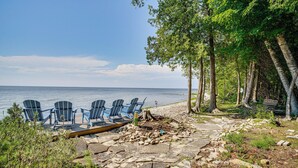 Un espace aménagé au bord de la plage, avec des fauteuils Adirondack, une terrasse en bois et un chemin de pierre menant à l’eau.