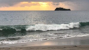 A beach with waves approaching the shore and a distant island under a cloudy sky. - 2min to Beach Rooftop Terrace 360 Views Pool BBQ - Casa Cazenovia 3BR (Tempate)