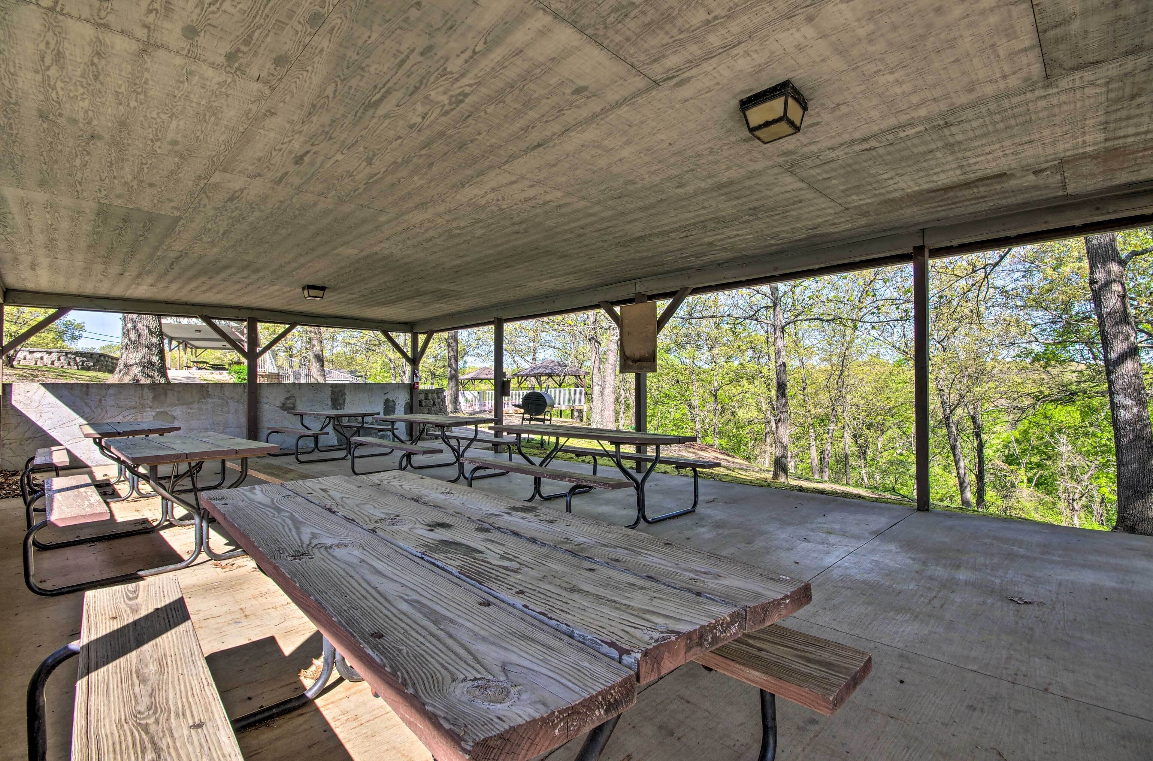 An outdoor covered picnic area with picnic tables and benches, surrounded by trees.