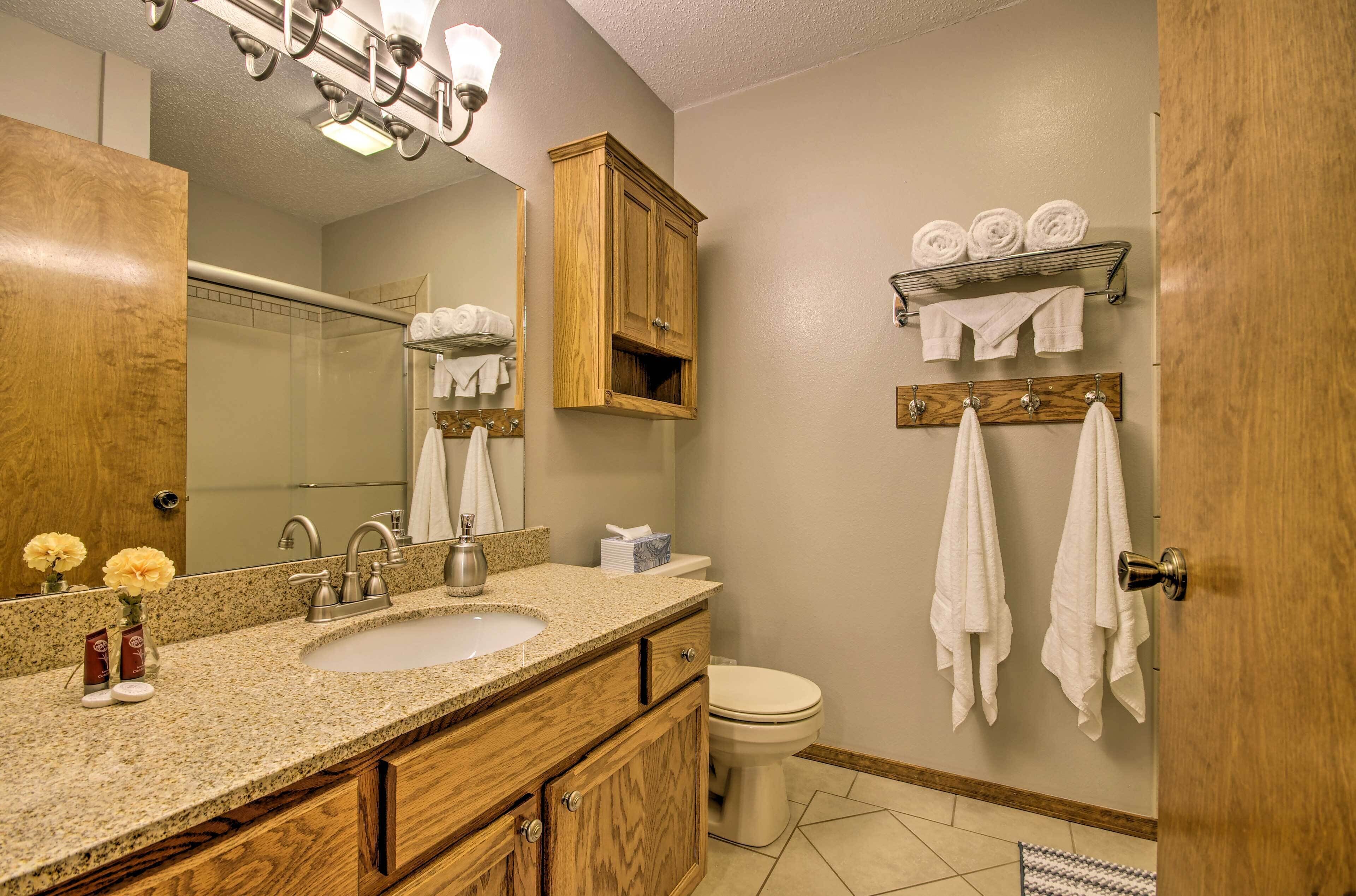 A bathroom with two sinks, a mirror, wooden cabinets, a toilet, and towels hung on hooks.