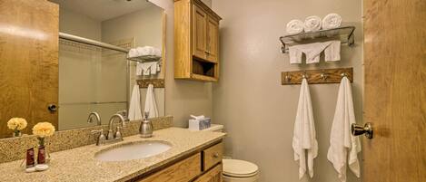 A bathroom with two sinks, a mirror, wooden cabinets, a toilet, and towels hung on hooks.