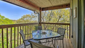 A covered outdoor area with a glass table and chairs, surrounded by a wooden deck and railing, overlooking a forested area. - Cozy Branson Getaway ~ 2 Mi to Silver Dollar City! (Branson West)