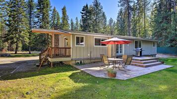 A single-story cabin with a deck, a patio with a table and chairs, and a red umbrella.