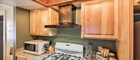 A kitchen with wooden cabinets, a microwave, a stove, and various utensils.