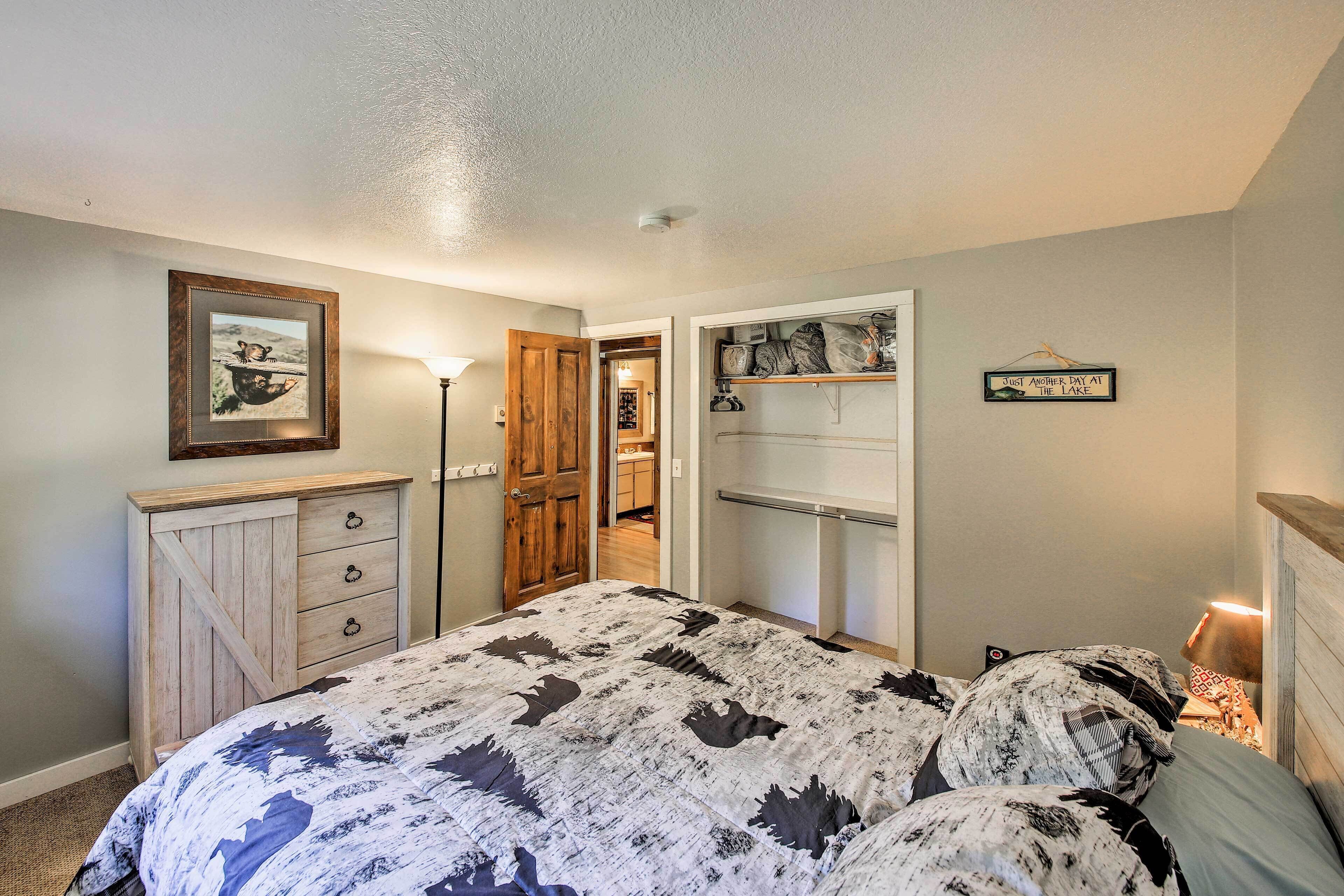 A bedroom with a bed, a dresser, a wardrobe, a door leading to a bathroom, and a wall with a framed picture and a sign.