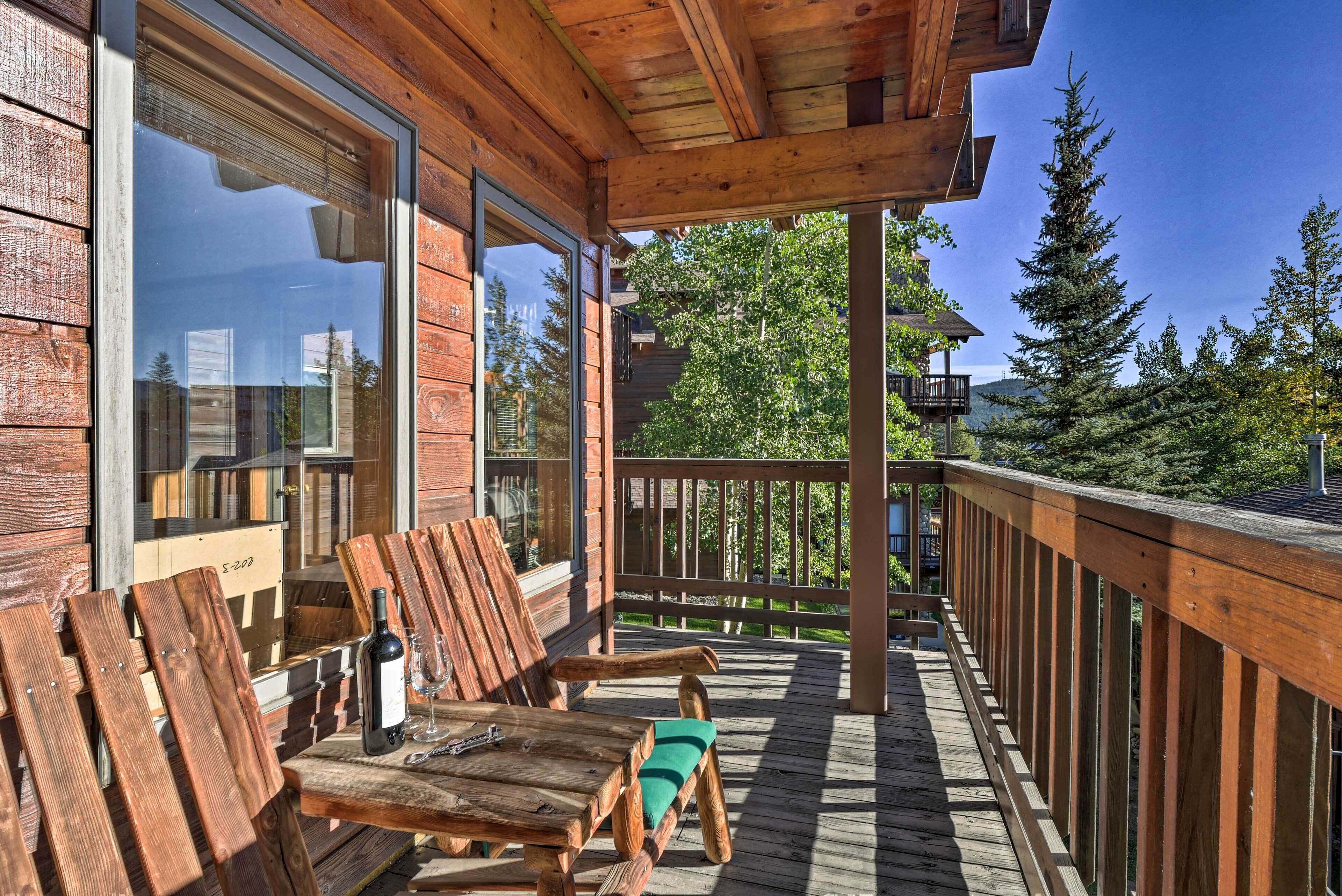 A wooden deck with a wooden table and chairs, a bottle of wine, and a glass.