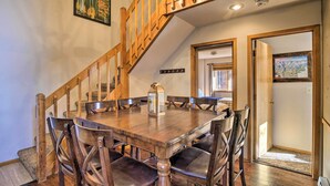 A dining area with a wooden table and chairs, a chandelier, and a staircase.