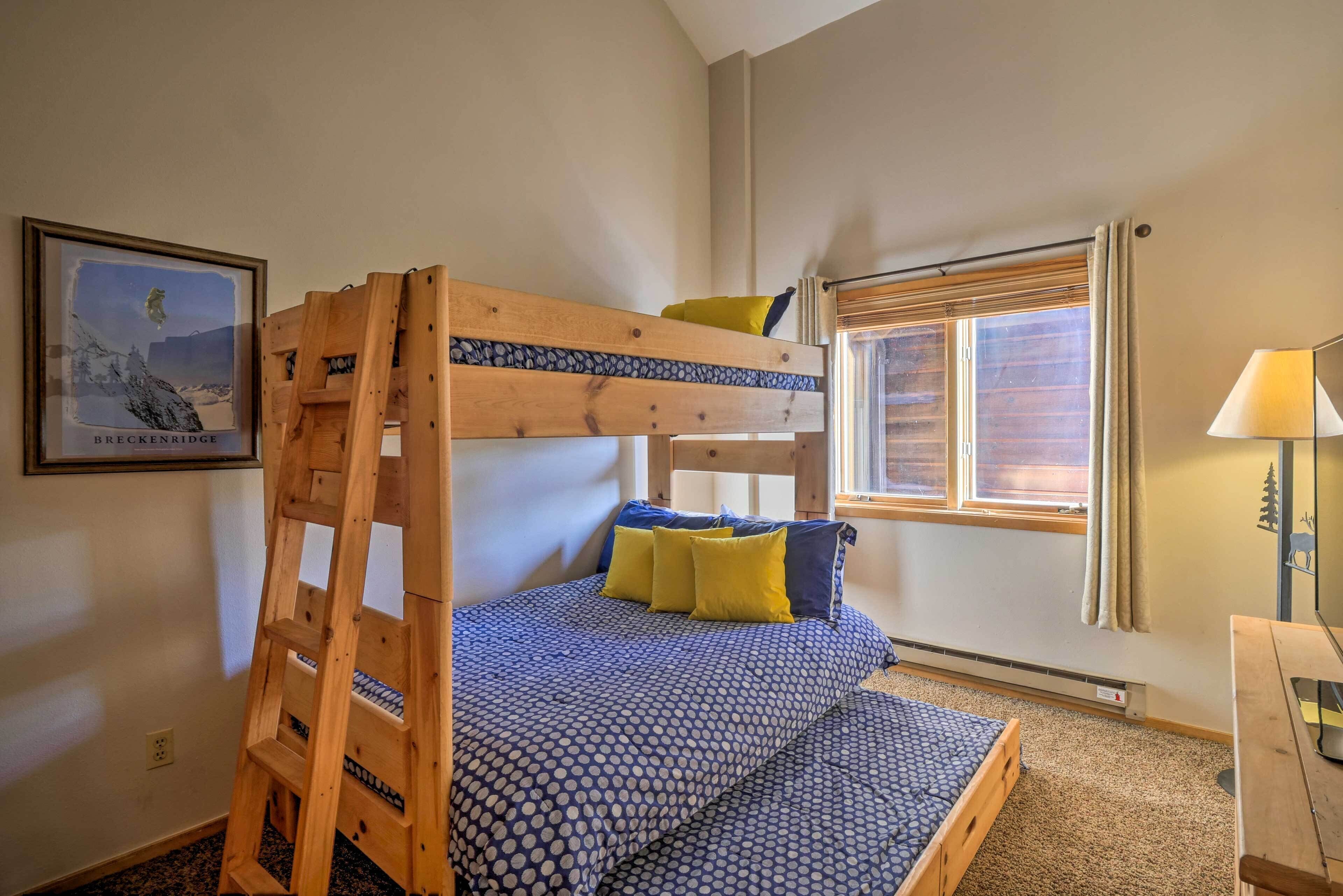 Ein Stockbett mit Holzleiter, ein gerahmtes Bild an der Wand, ein Fenster mit Vorhängen und ein Nachttisch mit Lampe.